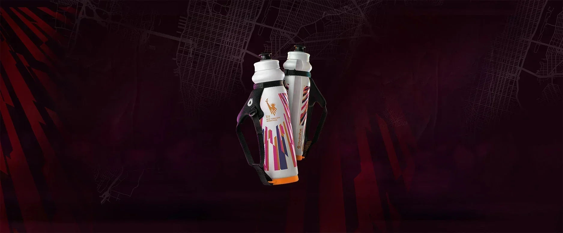 Displays two white HydraPak reusable water bottles equipped with black hand straps and orange bases. The bottles are decorated with colorful diagonal stripes in pink, orange, and blue, and prominently feature the TCS New York City Marathon logo.