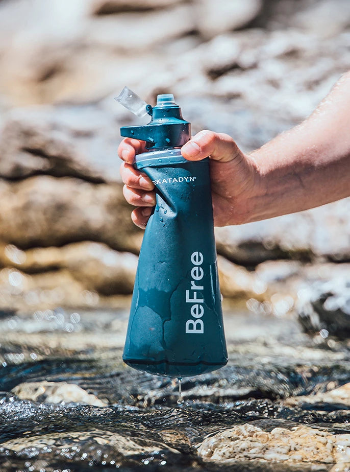 A hiker using the Katadyn BeFree filtration system with HydraPak's flexible, squeezable soft flask to filter water directly from a mountain stream.