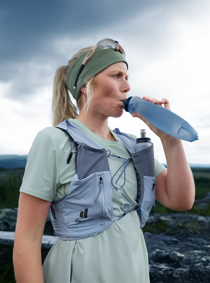 A trail runner hydrating with a deuter Streamer soft flask while wearing a deuter Traick running vest.