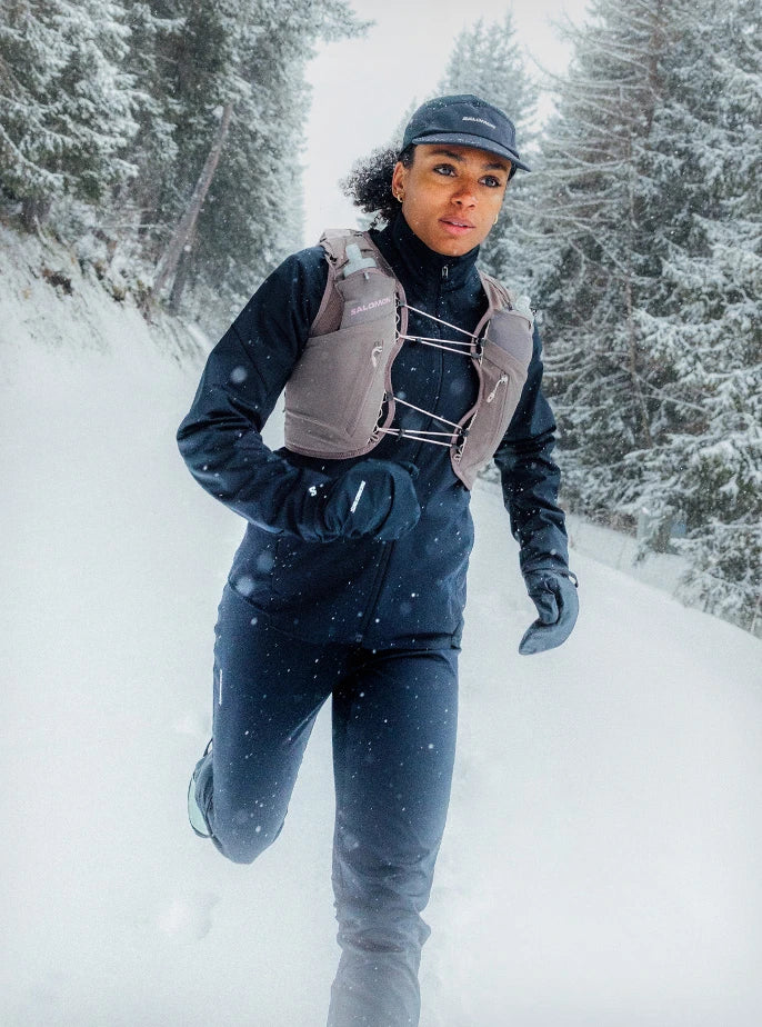 Close-up of a trail runner navigating a winter path while wearing a Salomon running vest equipped with HydraPak soft flasks.