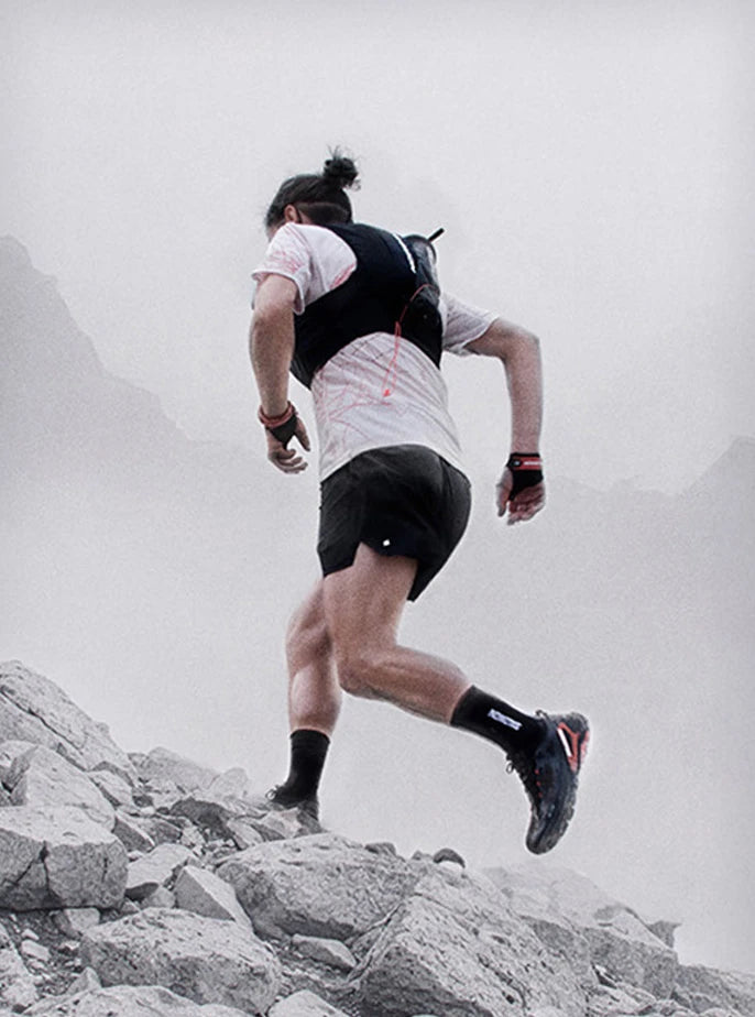 Low-angle view of an athlete running uphill on technical alpine terrain wearing a Salomon S/LAB hydration vest with soft flasks.