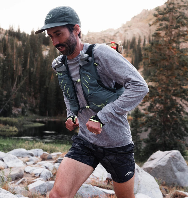 A man trail running over rocky alpine terrain wearing an Osprey hydration vest with two soft flasks in the front pockets.