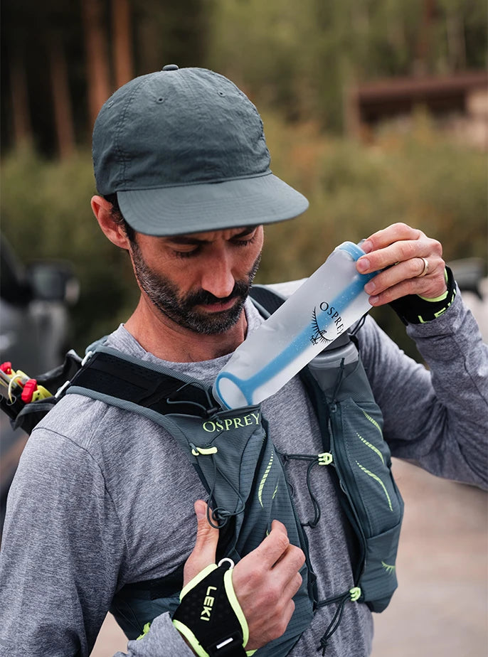 Close-up of a trail runner loading an Osprey 500mL Soft Flask into his hydration pack, clearly displaying the internal blue WingStay™ Removable Flask Stabilizer.