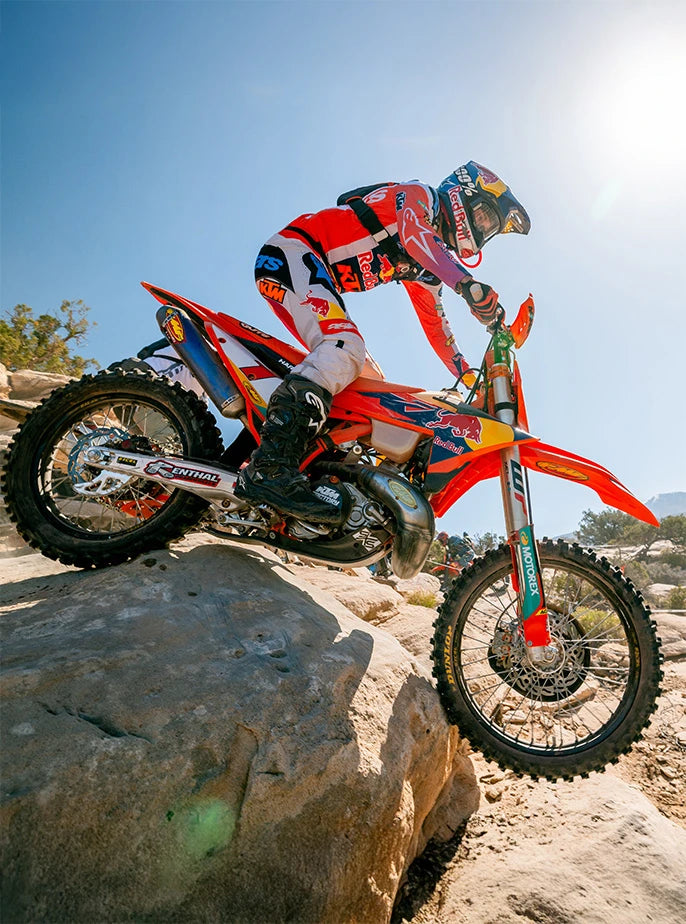 Low-angle action shot of a Red Bull KTM motocross rider descending a massive rock face with a USWE hydration system.