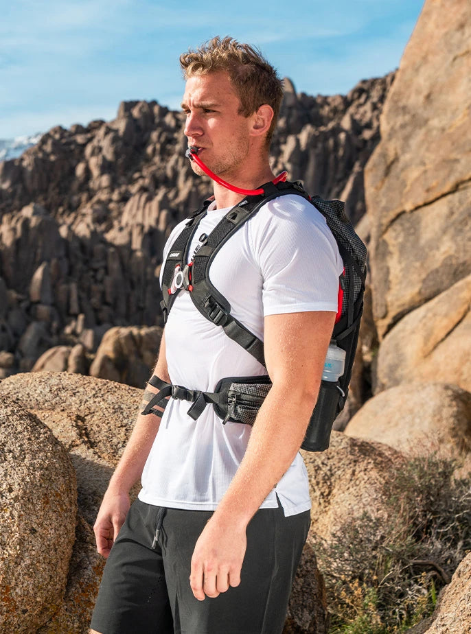 Side profile of an outdoor athlete using USWE’s No Dancing Monkey™ harness pack equipped with HydraPak’s signature red drink tube and side bottle storage.