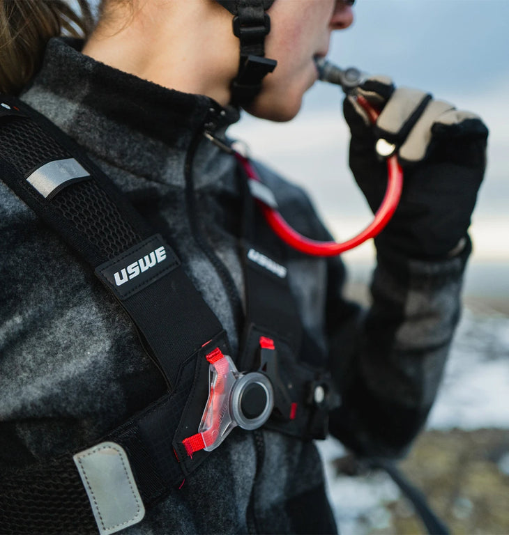 Detailed shot of USWE’s No Dancing Monkey™ chest harness featuring HydraPak’s signature red hydration tube and bite valve.